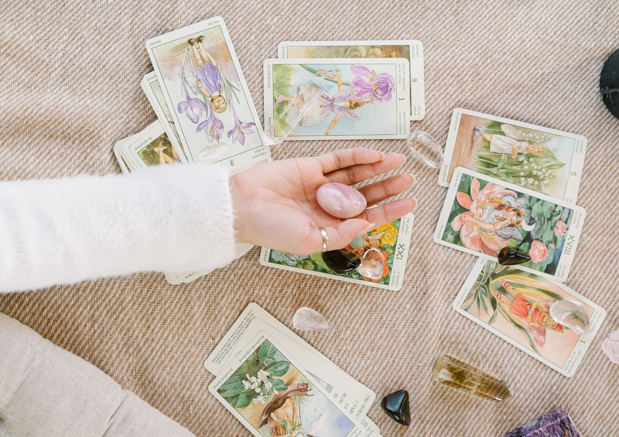 Persona sosteniendo una piedra mineral mientras se pueden apreciar en la mesa las cartas del tarot que hay